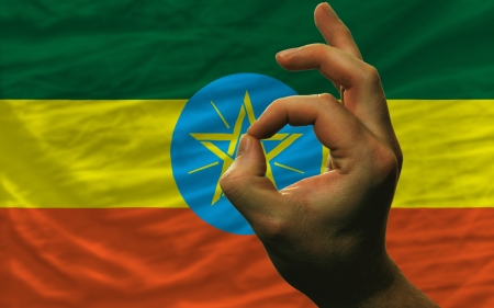 man showing excellence or ok gesture in front of complete wavy ethiopia national flag of  symbolizing best quality, positivity and succesの写真素材