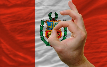man showing excellence or ok gesture in front of complete wavy peru national flag symbolizing best quality, positivity and succesの写真素材