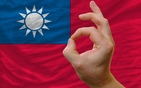 man showing excellence or ok gesture in front of complete wavy taiwan national flag symbolizing best quality, positivity and succesの写真素材