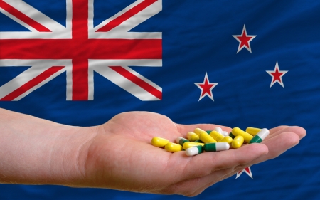 man holding capsules in front of complete wavy national flag of new zealand symbolizing health, medicine, cure, vitamines and healthy lifeの写真素材