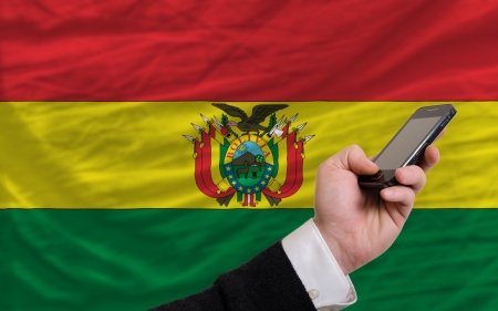 man holding cell phone in front national flag of bolivia symbolizing mobile communication and telecommunicationの写真素材