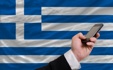 man holding cell phone in front national flag of greece symbolizing mobile communication and telecommunicationの写真素材