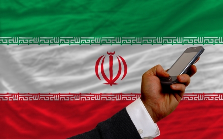 man holding cell phone in front national flag of iran symbolizing mobile communication and telecommunicationの写真素材