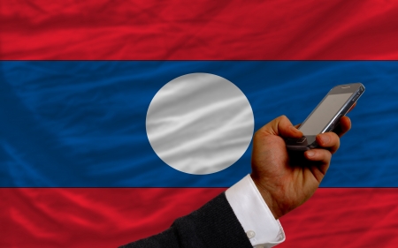 man holding cell phone in front national flag of laos symbolizing mobile communication and telecommunicationの写真素材