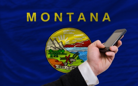man holding cell phone in front flag of us state of montana symbolizing mobile communication and telecommunicationの写真素材