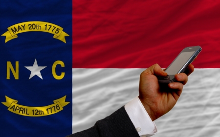 man holding cell phone in front flag of us state of north carolina symbolizing mobile communication and telecommunicationの写真素材