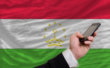 man holding cell phone in front national flag of tajikistan symbolizing mobile communication and telecommunicationの写真素材