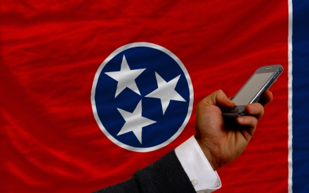 man holding cell phone in front flag of us state of tennessee symbolizing mobile communication and telecommunicationの写真素材