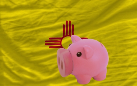 Piggy rich bank in front of flag of us state of new mexico symbolizing saving and accumulating funds as good financial habitの写真素材
