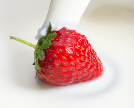 milk or cream poured on fresh red strawberry, close upの写真素材