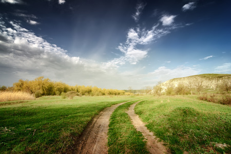 vintage road through fields with green grass and blue sky with cloudsの写真素材