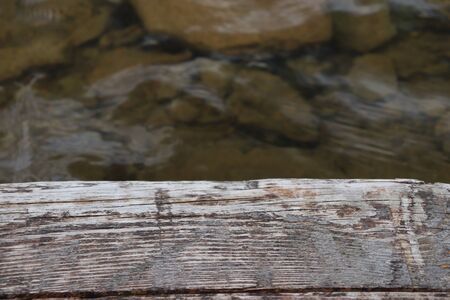 Blades of grass on the background of the old wooden floor, near the clear water of the lake, visible stonesの写真素材