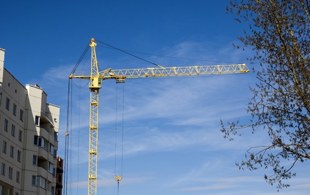 Construction crane above tall houses against the blue sky, building
