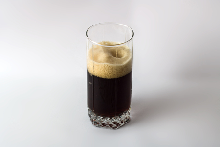 Dark beer in a glass with foam on a gray background with a shadowの写真素材