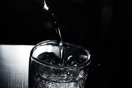 Water pours into a glass in the dark close upの写真素材