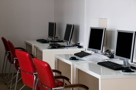 Computers on tables and red chairs in the computer room close up