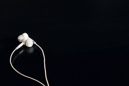 White headphones on a black wooden table, copy space