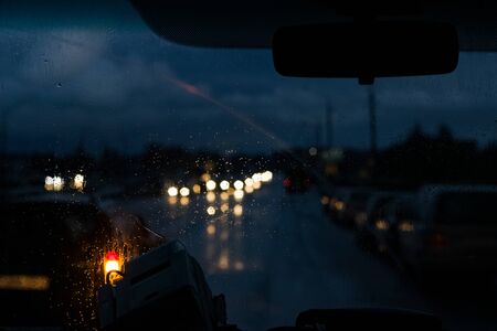 Car front window with raindrops and road with cars at nightの写真素材