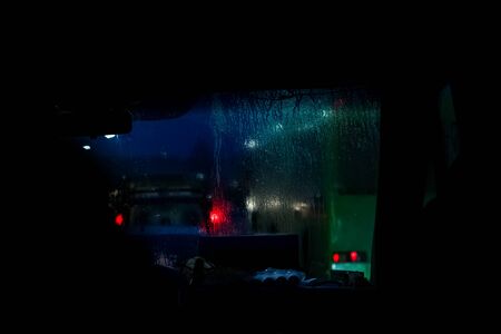 Car front window with raindrops and road with cars at nightの写真素材