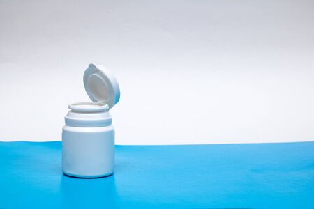 White jar with pills on a blue background, copy space