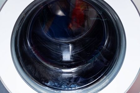 Dark laundry washing in machine drum close up, background