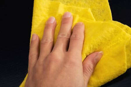 Yellow rag in the hand close up on black wooden tableの写真素材