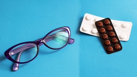 Glasses and packs of pills on a blue background