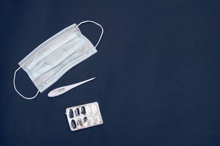 Medical face masks, thermometer and tablets on a gray background