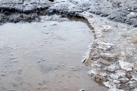 Frozen puddle in the road close up with water
