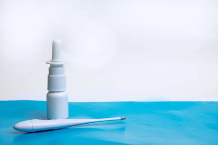 Drops for nose and electronic thermometer on a blue table, copy space