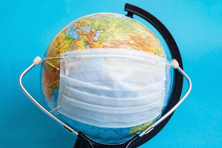 Globe in medical protective mask and stethoscope on blue background close upの写真素材
