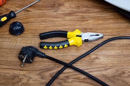 Pliers and wire with plug on wooden background close up