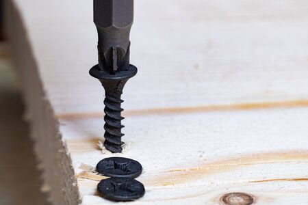 Screwing a screw into a wooden board close up
