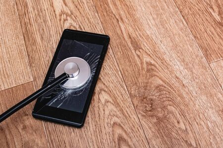 Stethoscope on a broken phone display on wooden background, copy spaceの写真素材