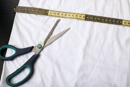 Measuring tape and scissors on white fabric close up