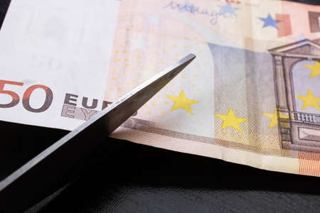 Scissors cut a euro bill close up on black backgroundの写真素材
