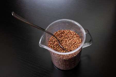 Buckwheat groats in a spoon on black background close up