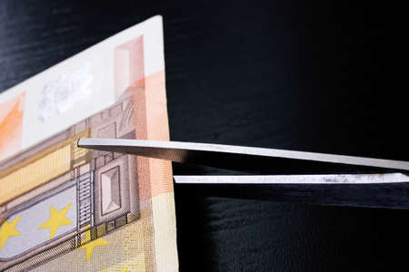 Scissors cut a euro bill close up on black backgroundの写真素材