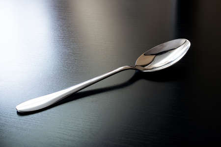 Metal spoon on black wooden table close up