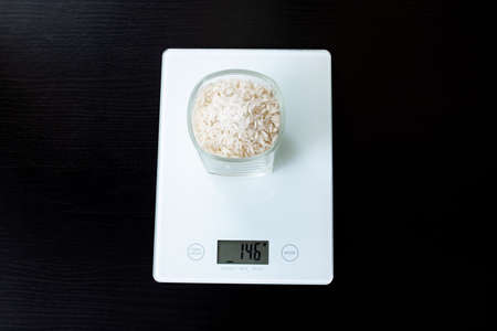 Glass with rice on electronic scales on a wooden tableの写真素材