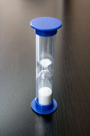 Hourglass with shadow on a wooden table close up