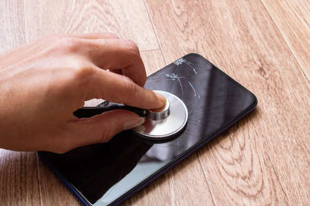 Stethoscope in hand and broken phone close up