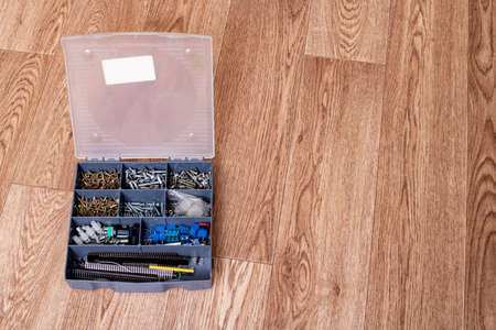 Various screws in a plastic box on a wooden table, copy space