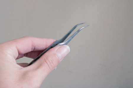 Tweezers in hand on a gray background close upの写真素材