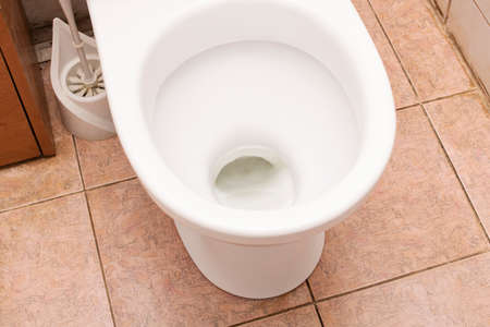 White toilet bowl and brush on the tile floorの写真素材