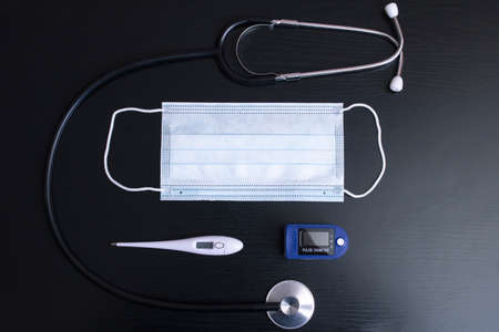 Mask, stethoscope, thermometer and oximeter on black background flat layの写真素材