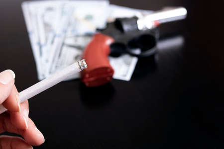 Gun, dollars and hand with a cigarette on a wooden table
