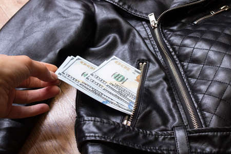 Hand pulls dollars out of jacket pocket close upの写真素材
