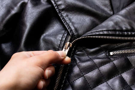 Hand unbuttones the lock of a black leather jacket