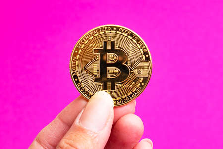 Bitcoinsa in hand on a pink background close upの写真素材
